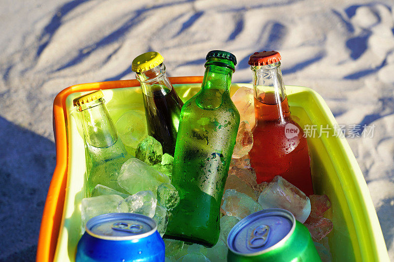苏打饮料和装满冰块的冷藏箱在沙滩上。