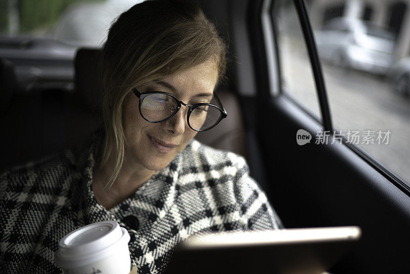 女商人在出租车里工作，用着平板电脑，喝着咖啡