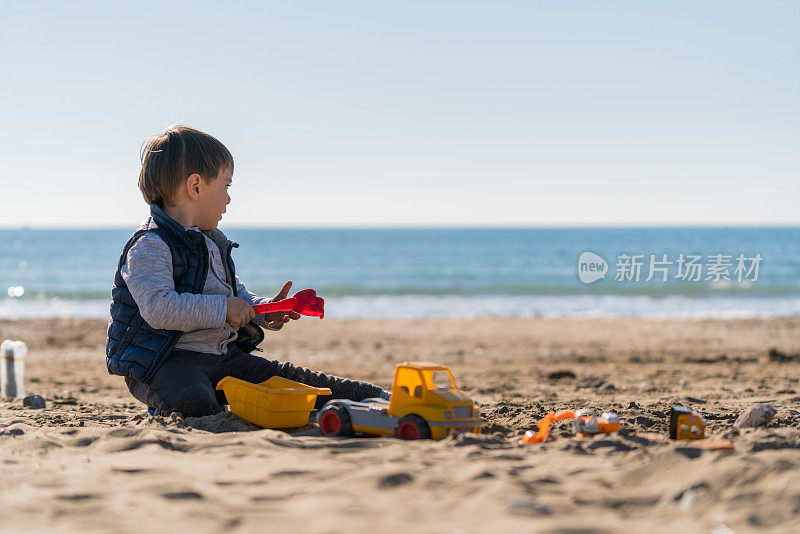 男孩在海滩上玩玩具卡车