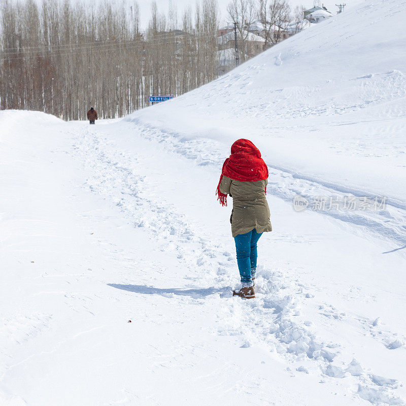 成年妇女穿着暖和的衣服在雪地上行走在农村