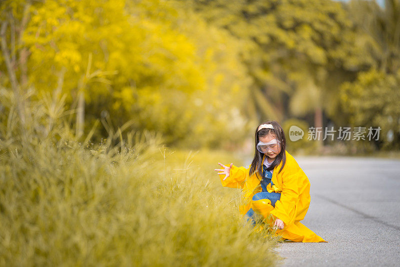 一个亚洲的中国女孩穿着雨衣和农家鞋在农场的草地上玩耍。