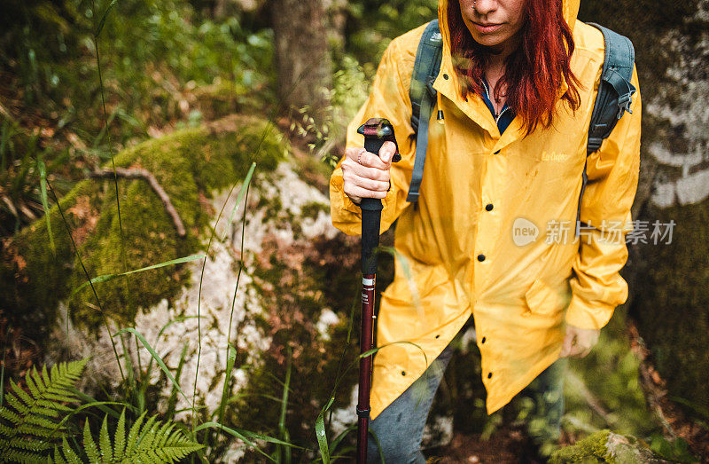 穿着雨衣的女背包客在露珠中徒步穿越森林