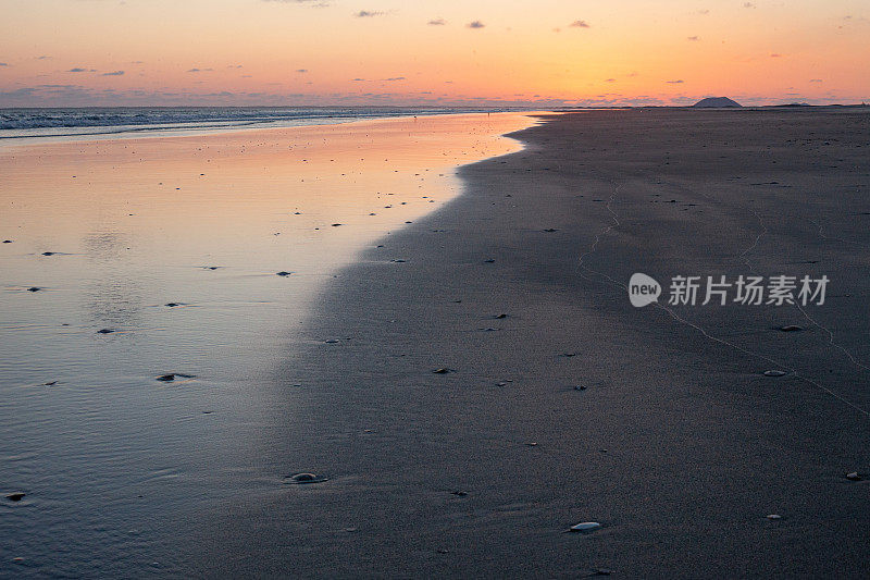 在日落后的海滩上，橙色的辉光在沙滩上反射出浅浅的海浪