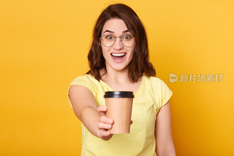 照片中，年轻漂亮的女性兴奋地递给外卖咖啡，将热饮递给她的朋友，脸上带着惊讶的表情，微笑着直视镜头。人。