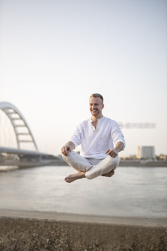 年轻美丽的男子在半空中沉思的肖像，漂浮在户外地面上，坐在莲花姿势，莲花身