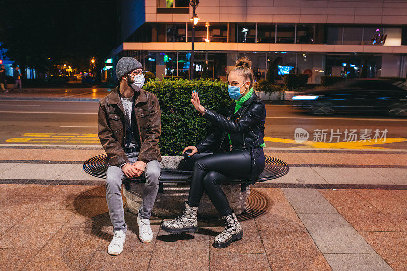 年轻的白人朋友们戴着N-95面具在汽车站边聊天边等车