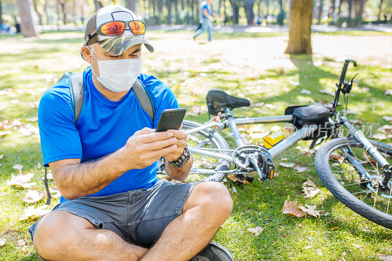 一名男子戴着防护面具坐在草地上用智能手机