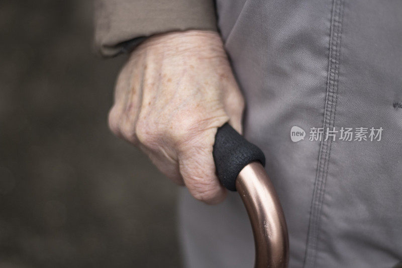 一位老妇人的手拄着拐杖。