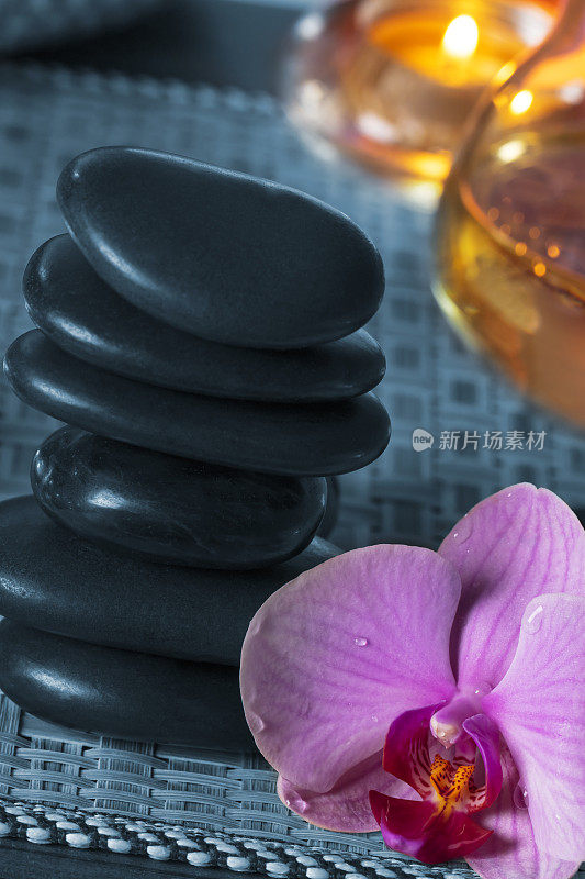美容spa概念-黑色按摩石，兰花花和油在木垫子上