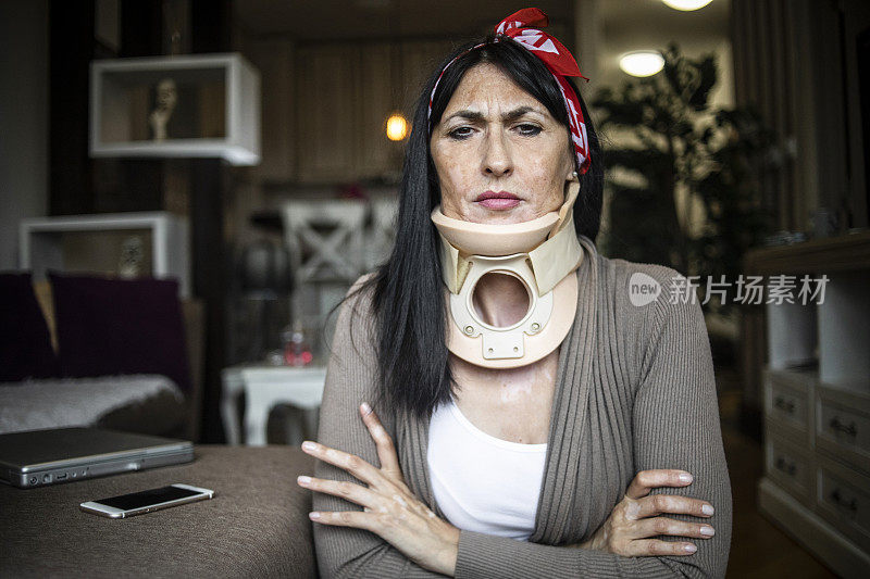 一名妇女戴着颈椎手术颈圈在家进行日常活动——一名黑发的老年妇女在颈椎受伤后坐在家里，正在成功康复