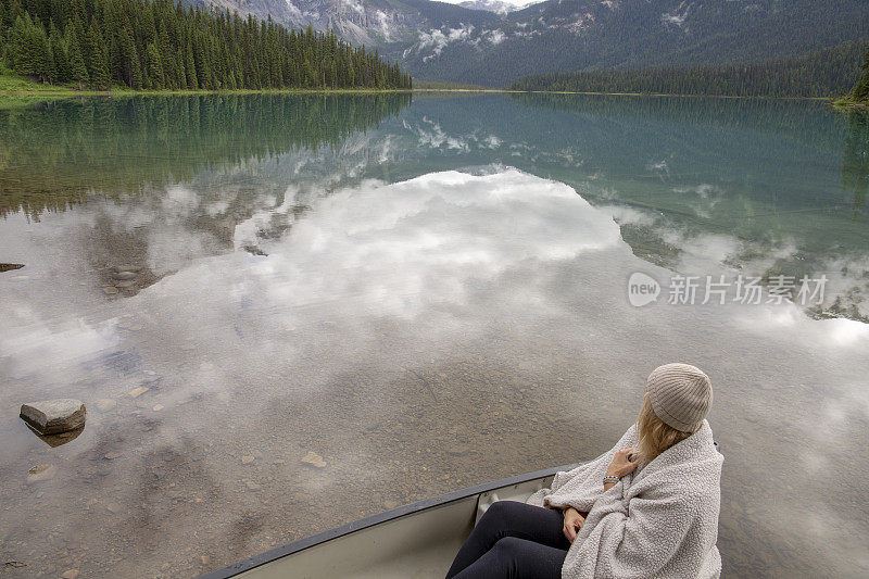 一个裹着毯子的女人坐在高山湖上的小船上