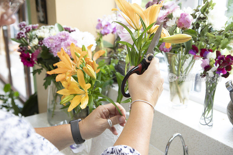 特写的女性手修剪叶子一束百合在一个花瓶