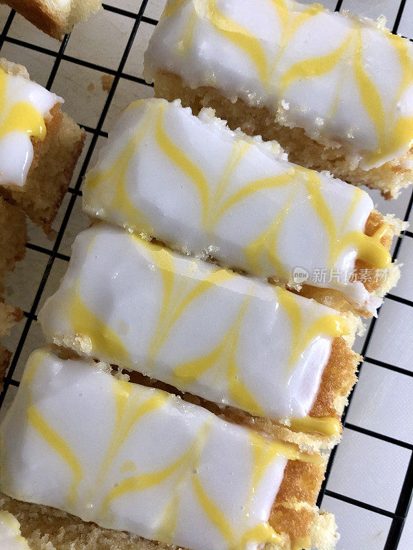 在金属冷却架上放置自制的柠檬托盘烘焙蛋糕片，上面覆盖着白色的方糖糖霜和黄色的羽毛柠檬味糖霜