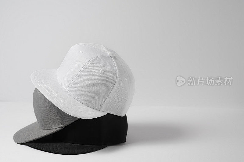 特写镜头的三个空白单色白色，灰色和黑色棒球帽孤立在光的背景