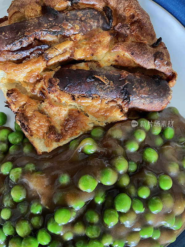 全框图像自制的传统英国蟾蜍在洞食谱与多汁的猪肉香肠，约克郡布丁面糊和焦糖洋葱，青豆和肉汁在白色盘子与蓝色边缘，提高视野