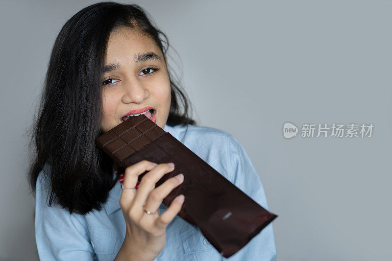 快乐的印度女孩手里拿着一块黑巧克力，咬了一口。