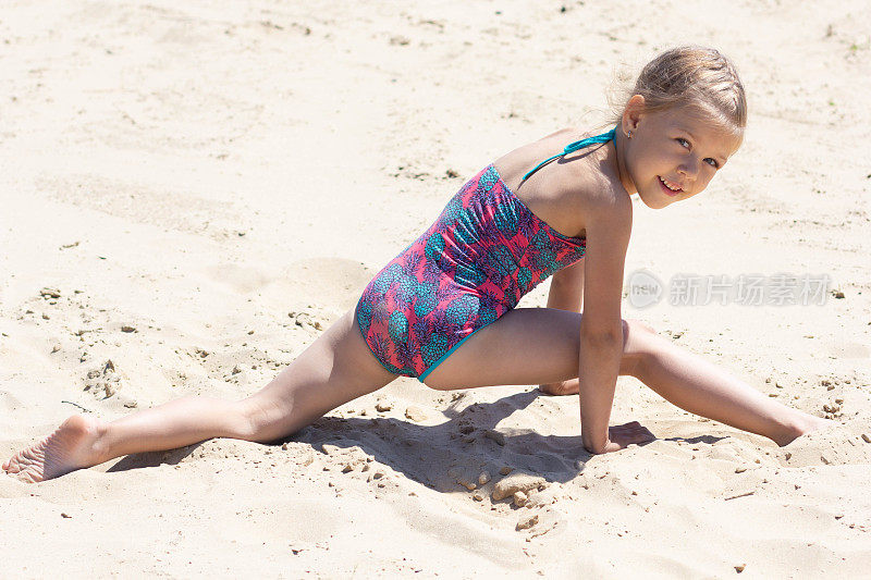 五岁的白人小女孩穿着泳装在沙滩上做腿在夏天