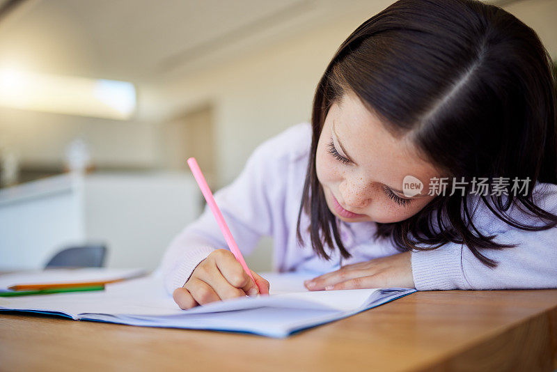 小女生在餐桌上做作业。聪明的小学生在笔记本上写字