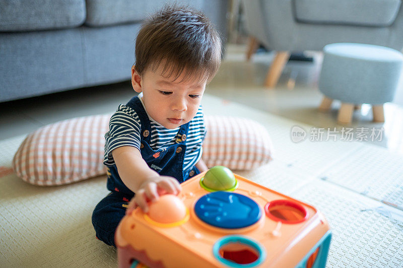 小男孩坐在地板上玩小球，把它们放在客厅的活动箱里