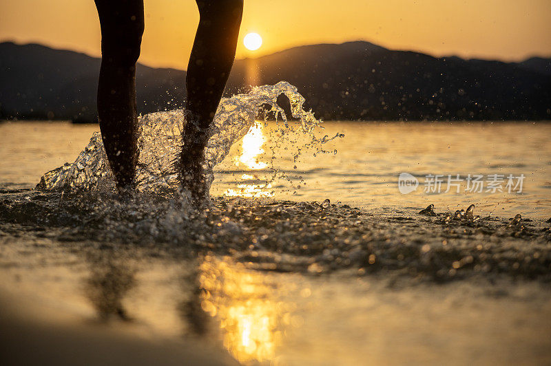 女性的腿走进水中在日落的海滩