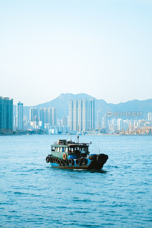 在摩天大楼林立的香港城市景观面前，一艘船在海上航行