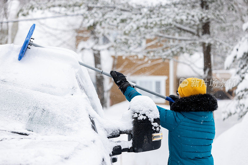 一名年轻女子在暴风雪后清理车上的积雪