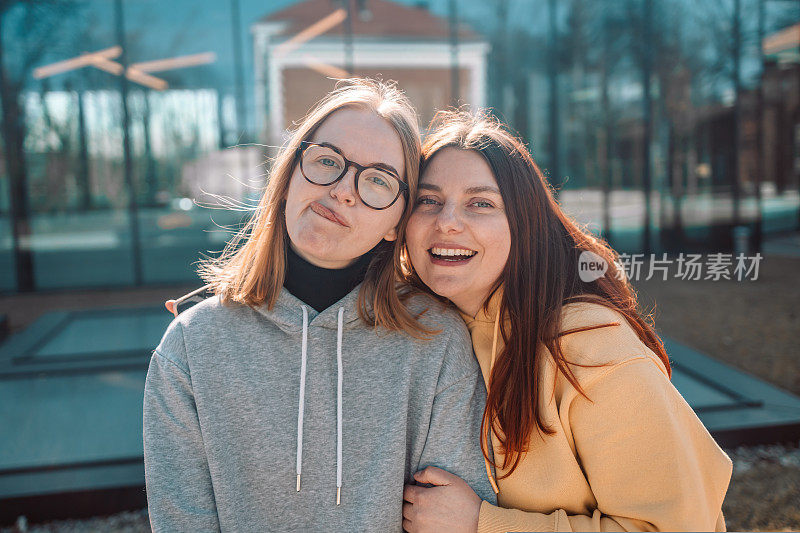 两个年轻的时尚女性微笑着用智能手机自拍自画像，表现出积极的情绪