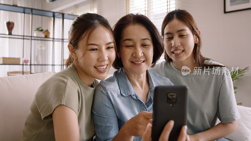 一群亚洲人年轻的成年妇女和中年母亲看着网络摄像头摄像头虚拟谈话在线facetime视频电话舒适地坐在家里的沙发上。老妈妈喜欢和孩子一起放松微笑自拍。