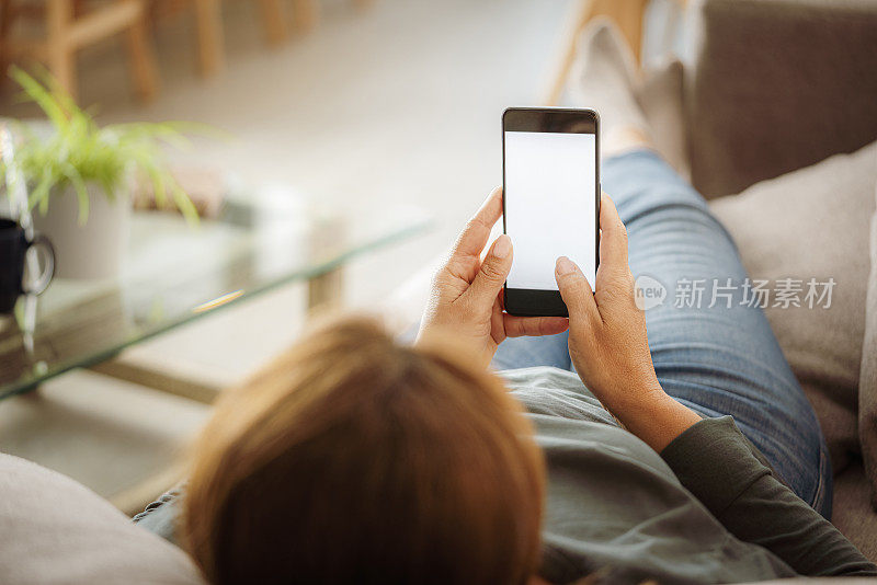 放松的女人躺在沙发上使用电话的后视图