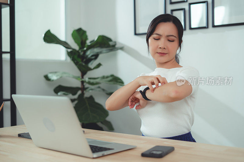 亚洲妇女刺激瘙痒，干皮肤抓她的皮肤坐在家里办公室。