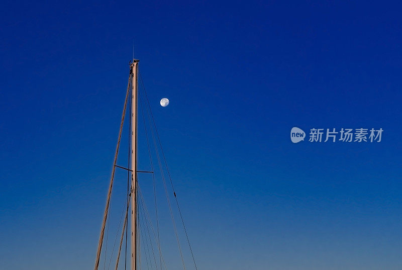满月和帆船桅杆在暮色中深蓝色的天空