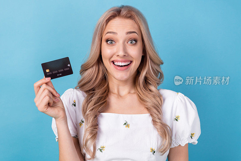 疯狂有趣的反应的照片，印象深刻的女孩拿着塑料银行卡单一银行收入，没有税，孤立在蓝色背景