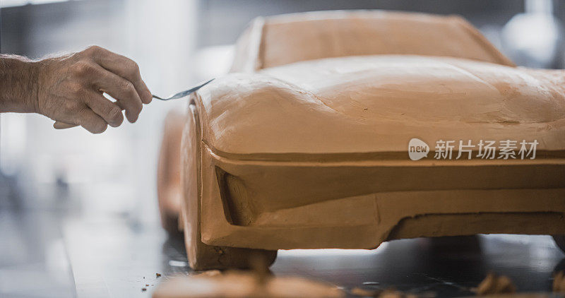 近距离在车辆生产的第一步工作的专家建模，创建一个微型比例的3D汽车模型的粘土。一位匿名男子正在小心地修整一辆概念车的表面