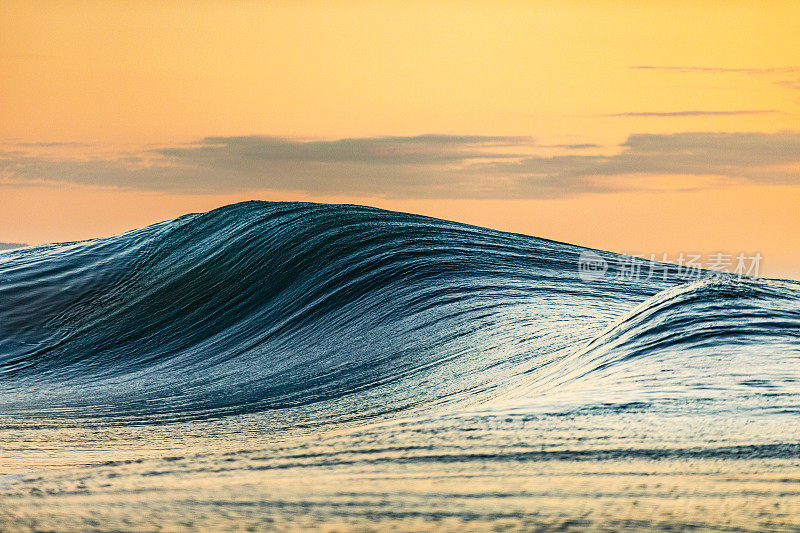 光滑弯曲的波浪在海洋与金色的天空黄昏