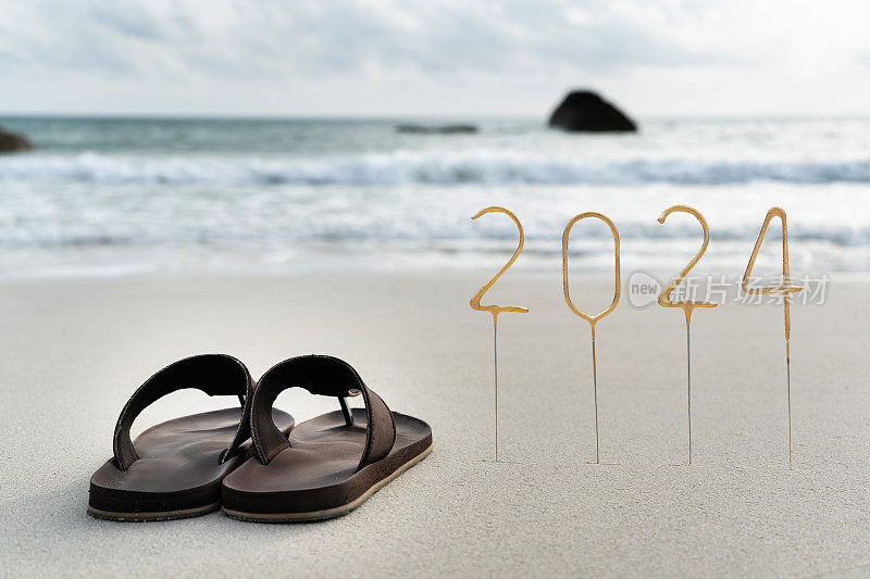 穿着人字拖在空旷的沙滩上为即将到来的新年写上2024年的数字