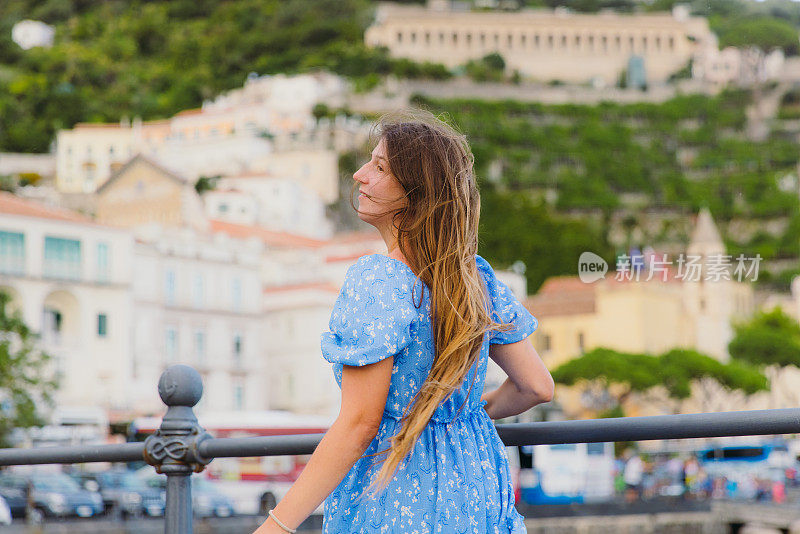 穿着蓝裙的快乐女子在海港漫步，欣赏阿马尔菲的美景