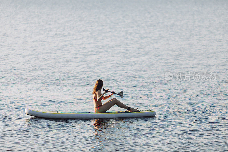 一个女人在日落时分在湖边玩桨板
