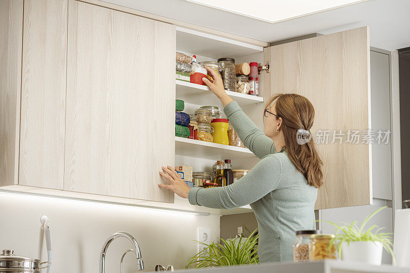 妇女在厨房上层的橱柜里整理食品杂货