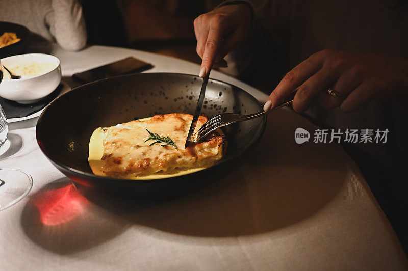 一个女人的手在一家豪华餐厅吃美味的千层面的特写。