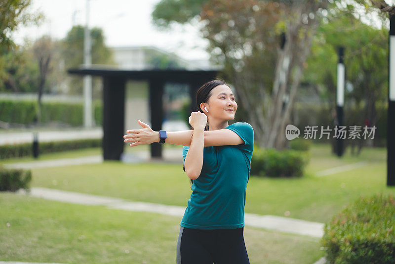亚洲妇女戴着耳机在公园里伸展和锻炼。