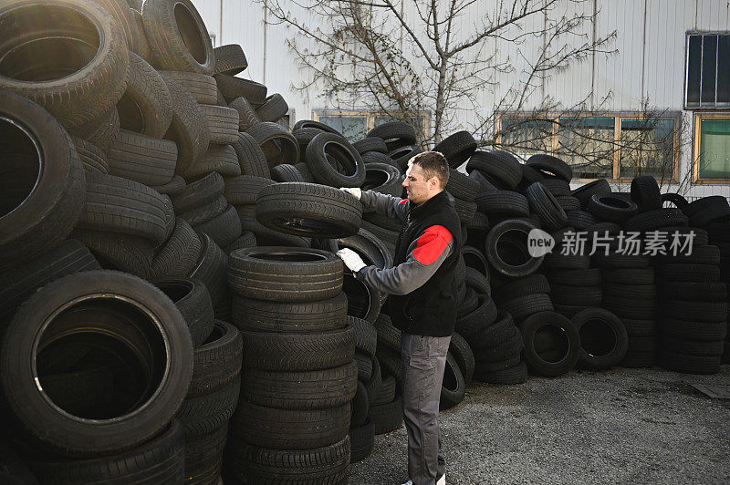 搬运废旧轮胎准备回收的男子。成堆的旧轮胎和车轮用于回收橡胶。