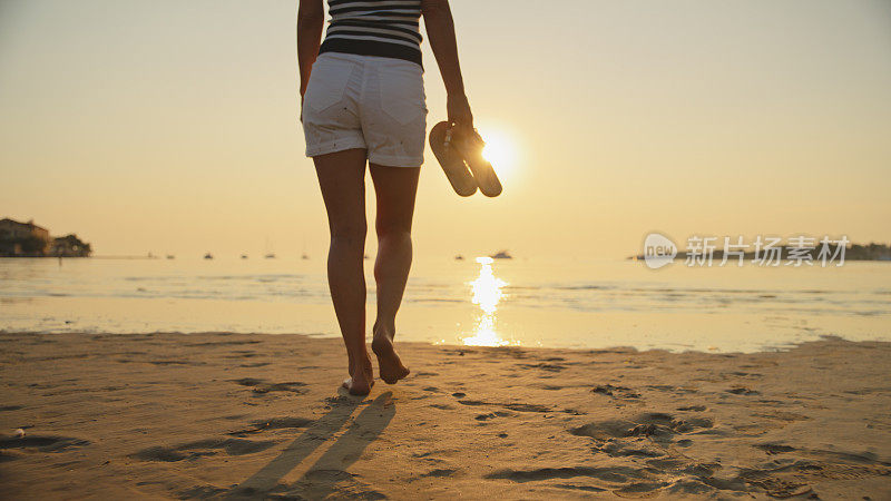日落时分，女子穿着拖鞋在沙滩上朝着天空走去