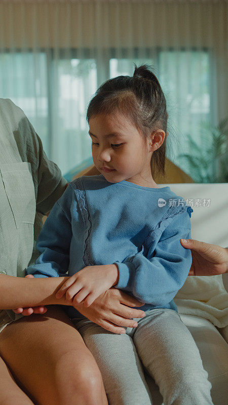 一位女医生正在家里检查一个生病发高烧的女孩的皮肤。生病女孩因为身体状况和家庭健康和她妈妈住在一起。垂直的屏幕。