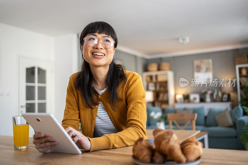 一位中年日本妇女早餐吃黄油牛角面包，然后在她的平板电脑上翻看每日新闻