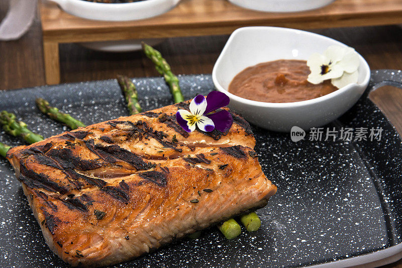 餐厅餐桌上的烤三文鱼配以芦笋、酱汁和调味料，并以鲜花装饰