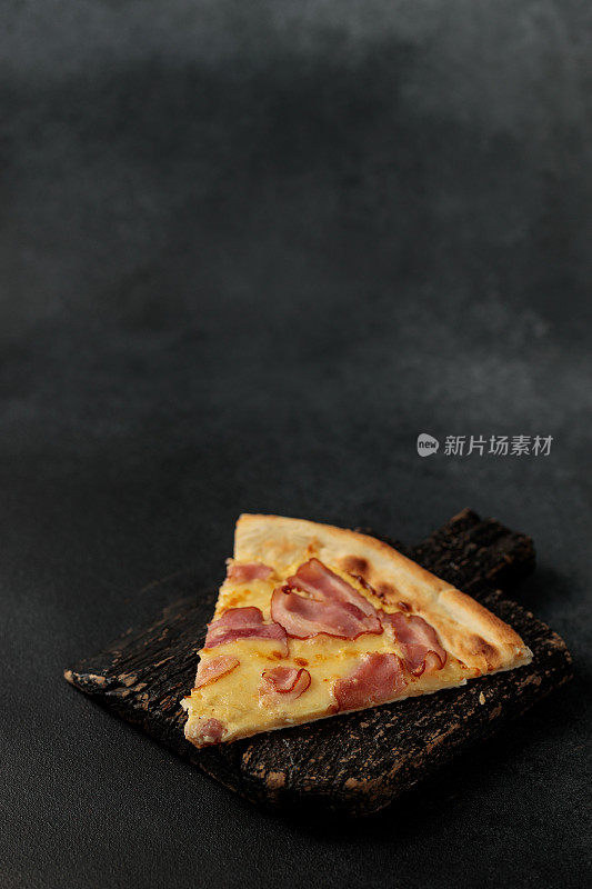 黑色砧板上的一块烤披萨。黑色背景。文本空间