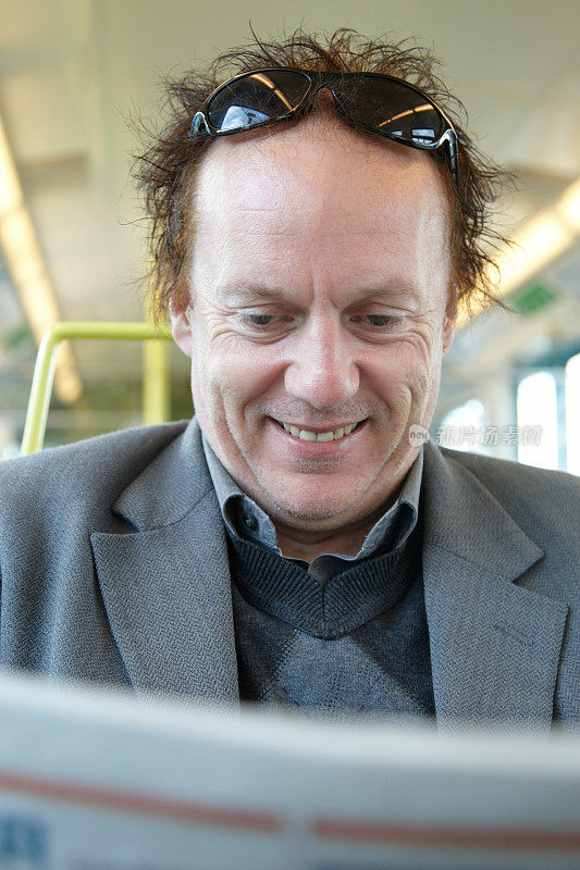 微笑的中年男子在火车上看报纸