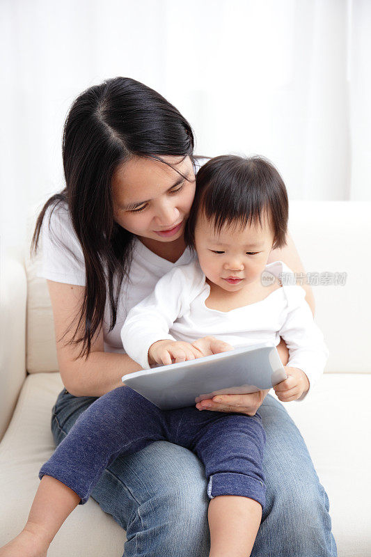亚洲母亲与孩子在她的腿上一起使用平板电脑