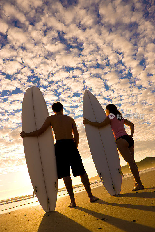 日出时分，两个冲浪者站在海滩上