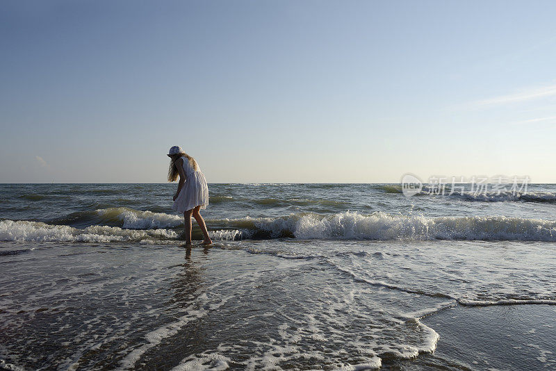 穿着白色背心裙的女孩在海边寻找贝壳